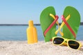 Stylish flip flops, sunglasses and sun protection cream on sandy beach Royalty Free Stock Photo