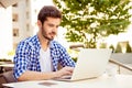 Stylish freelancer is working on his computer, sitting outdoors