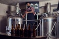 Stylish full bearded Indian man in a fleece shirt and apron controls the brewing process, standing near beer tank in the Royalty Free Stock Photo