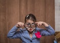 stylish funny little girl looking toward trough the magnified glasses on brown curtains background inside the room