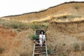 Stylish girl in fashionable look sitting on wooden stairs on beach cliff at sea in sunny light. Happy young boho woman in hat with Royalty Free Stock Photo