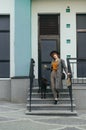 Stylish girl goes down the dog with stairs and looks into the camera. Cute lady in stylish clothes and hat poses on camera with a