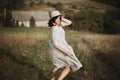 Stylish girl in linen dress running barefoot among herbs and wildflowers in sunny field in mountains. Boho woman relaxing in Royalty Free Stock Photo