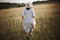 Stylish girl in linen dress running among herbs and wildflowers in sunny meadow in mountains. Boho woman relaxing in countryside, Royalty Free Stock Photo