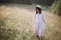 Stylish girl in linen dress walking among wildflowers in sunny meadow in mountains. Boho woman relaxing in countryside flowers at Royalty Free Stock Photo