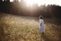 Stylish girl in linen dress walking among wildflowers in sunny meadow in mountains. Boho woman relaxing in countryside flowers at Royalty Free Stock Photo