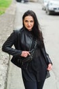 Stylish girl posing in street in fashionable outfit. Woman in black leather jacket and small leather fanny pack Royalty Free Stock Photo