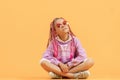 Stylish girl in rounded glasses with pink dreadlocks sitting, looking at camera and posing on a yellow background Royalty Free Stock Photo