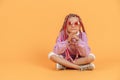 Stylish girl in rounded glasses with pink dreadlocks sitting, looking at camera and posing on a yellow background Royalty Free Stock Photo