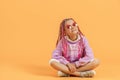 Stylish girl in rounded glasses with pink dreadlocks sitting, looking at camera and posing on a yellow background Royalty Free Stock Photo