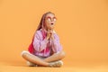 Stylish girl in rounded glasses with pink dreadlocks sitting, thinking, look up and posing on a yellow background Royalty Free Stock Photo