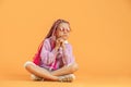 Stylish girl in rounded glasses with pink dreadlocks sitting, thinking and posing on a yellow background. Beauty Royalty Free Stock Photo