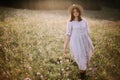 Stylish girl in rustic dress and hat walking among wildflowers in sunny meadow in mountains. Boho woman relaxing in countryside Royalty Free Stock Photo