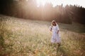 Stylish girl in rustic dress walking in wildflowers in sunny meadow in mountains. Boho woman relaxing in countryside flowers at Royalty Free Stock Photo