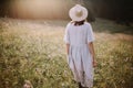 Stylish girl in rustic dress walking in wildflowers in sunny meadow in mountains. Boho woman relaxing in countryside flowers at Royalty Free Stock Photo