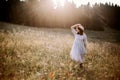 Stylish girl in rustic dress walking in wildflowers in sunny meadow in mountains. Boho woman relaxing in countryside flowers at Royalty Free Stock Photo