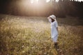 Stylish girl in rustic dress walking in wildflowers in sunny meadow in mountains. Boho woman relaxing in countryside flowers at Royalty Free Stock Photo