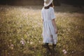 Stylish girl in rustic dress walking in wildflowers in sunny meadow in mountains. Boho woman relaxing in countryside flowers at Royalty Free Stock Photo