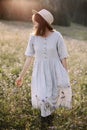 Stylish girl in rustic dress walking in wildflowers in sunny meadow in mountains. Boho woman relaxing in countryside flowers at Royalty Free Stock Photo