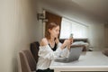 Stylish girl sitting at a desk with a laptop in apartments with stylish light interior, using a smartphone. Young female Royalty Free Stock Photo