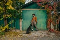 Stylish girl in vintage clothes posing with a dog on a background of green summer cottage in the autumn season. Autumn portrait of