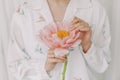 Stylish girl in white floral shirt gently holding peony flower in hands with jewelry. Sensual image. Beautiful young woman holding