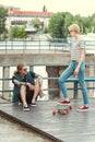 stylish girlfriend putting leg on skateboard and looking on tattooed boyfriend