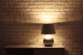 Stylish glowing night lamp on table near white brick wall. Space for text