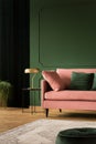 Stylish golden lamp on industrial table next to pink couch with emerald pillows in dark green living room interior,copy space on