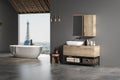 Stylish gray bathroom interior with concrete floor, window with city view, dark wall, white bathtub, and sink with vertical mirror Royalty Free Stock Photo