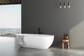 Stylish gray bathroom interior with white bathtub, concrete floor, window with city view, dark wall, white bathtub. 3 d rendering Royalty Free Stock Photo