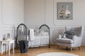 Stylish grey baby room with wooden crib, comfortable armchair and white table with books, real photo with copy space on the empty Royalty Free Stock Photo