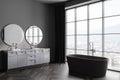 Stylish grey bathroom interior with bathtub and two sinks, panoramic window