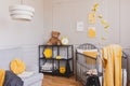 Stylish grey and yellow baby bedroom with crib and industrial black metal shelf