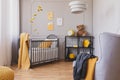 Stylish grey and yellow baby bedroom with crib and industrial black metal shelf