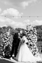 A stylish groom and a beautiful bride in a long dress stand near the arch Royalty Free Stock Photo