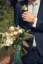 A stylish groom in a blue suit, green tie and white shirt touches a boutonniere of white roses and leaves Royalty Free Stock Photo