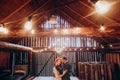 Stylish groom and happy bride hugging under retro bulbs lights in wooden barn. rustic wedding concept, space for text. newlyweds