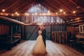 Stylish groom and happy bride hugging under retro bulbs lights in wooden barn. rustic wedding concept, space for text. newlyweds