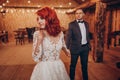 Stylish groom and happy bride posing under retro bulbs lights in wooden barn. rustic wedding concept, space for text. newlyweds