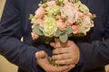 Stylish groom holds wedding bouquet. Young groom in a suit.