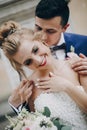 Stylish groom kissing sensually his happy bride in sunny european city street. Gorgeous wedding couple of newlyweds embracing at Royalty Free Stock Photo