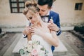 Stylish groom kissing sensually his happy bride in sunny european city street. Gorgeous wedding couple of newlyweds embracing at Royalty Free Stock Photo