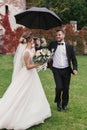 Stylish groom running under umbrella in rainy outdoor to Gorgeous bride and smiling. Sensual wedding couple having fun in rain. R Royalty Free Stock Photo