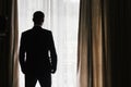 Stylish groom silhouette in suit posing at window light. Confide Royalty Free Stock Photo