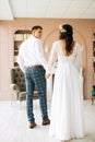 Stylish groom in a suit and a young bride in a wedding lace dress with a bouquet of flowers, sit together, hug, in the studio on Royalty Free Stock Photo