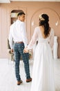 Stylish groom in a suit and a young bride in a wedding lace dress with a bouquet of flowers, sit together, hug, in the studio on Royalty Free Stock Photo
