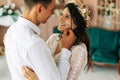 Stylish groom in a suit and a young bride in a wedding lace dress with a bouquet of flowers, sit together, hug, in the studio on Royalty Free Stock Photo