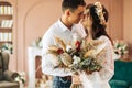 Stylish groom in a suit and a young bride in a wedding lace dress with a bouquet of flowers, sit together, hug, in the studio on Royalty Free Stock Photo