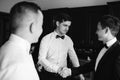 Stylish groomsmen helping happy groom getting ready in the morning